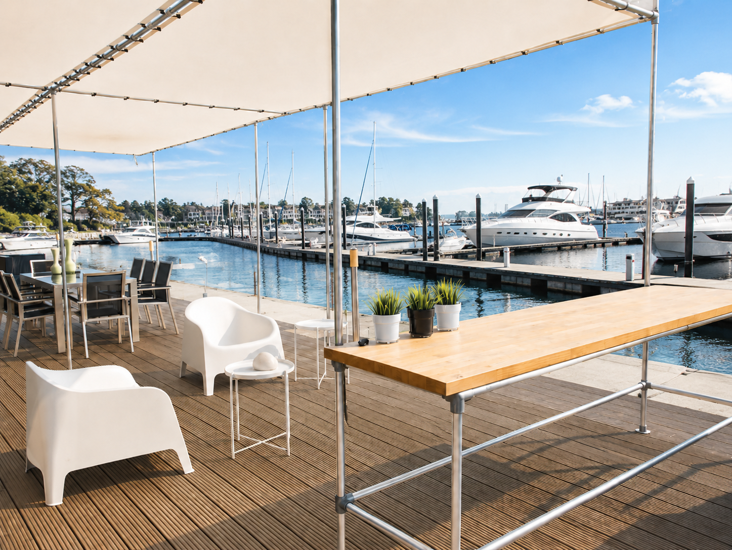 Terrasse en bois sous un auvent au port de plaisance. Fauteuils blancs modernes, table à manger et long comptoir en bois avec plantes en pot. À l'arrière-plan, voiliers et yachts sur les eaux bleues, ciel éclatant.