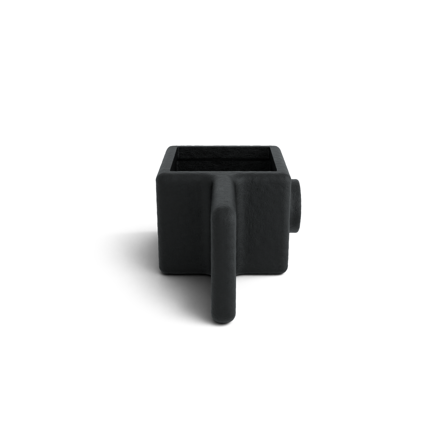 Un cache-pot carré, d’un noir profond et à la texture rugueuse, se détache sur un fond blanc. À l’avant, une protubérance plate et verticale forme une poignée ; à l’arrière, une forme cylindrique courte dépasse. Une ombre douce se dessine en dessous.